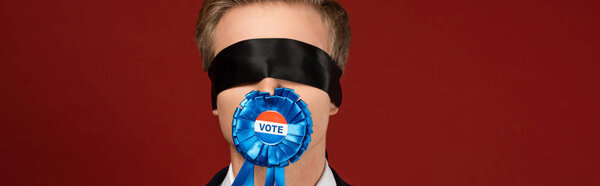 man with blindfold on eyes and badge with vote lettering in mouth on red background