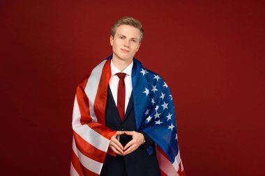 Kırmızı arka planda Amerikan bayrağı taşıyan gülümseyen adam.