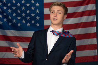 Amerikan bayrağı geçmişinde el kol hareketi yapan bir adam.