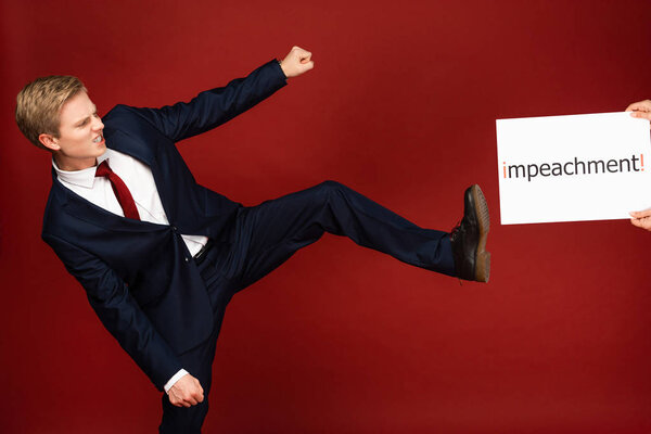 emotional man pushing with leg white card with impeachment lettering on red background