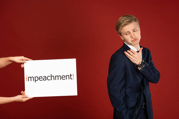 скептик рядом с белой картой с надписью импичмента на красном фоне
