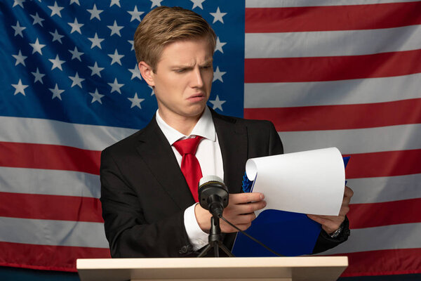 emotional man looking at clipboard on tribune on american flag background