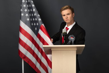 serious man on tribune with american flag on black background clipart