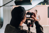 Selektivní zaměření kameramana s kamerou pracující s krásnou ženou ve fotostudiu
