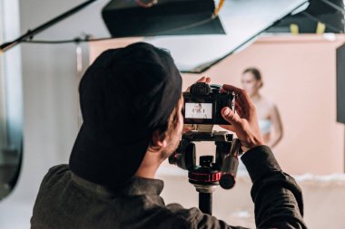Selective focus of videographer with camera working with beautiful woman in photo studio clipart