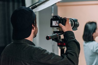 Rear view of videographer with assistant and model working in photo studio clipart