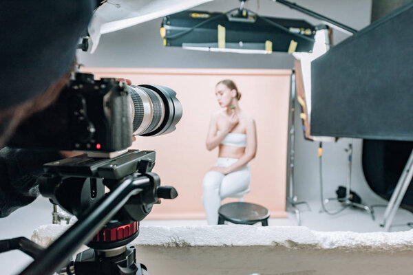 Selective focus of videographer with camera and model in photo studio with spotlights