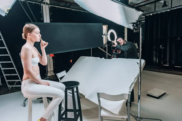 スポットライト付き写真スタジオでのビデオカメラマンのためのマッサージローラーでポーズ美しいモデル — ストック写真