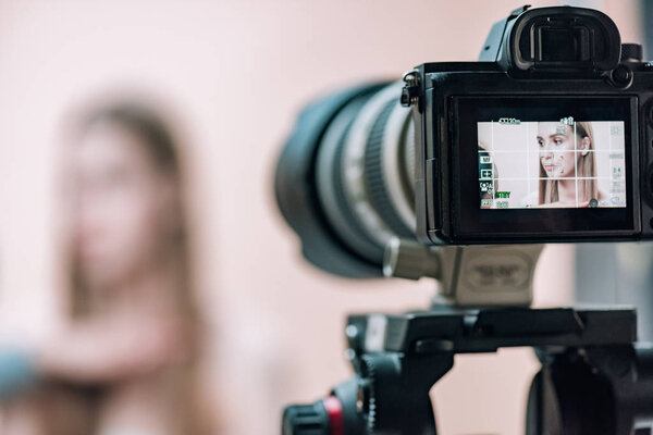 Selective focus of attractive model on camera display in photo studio