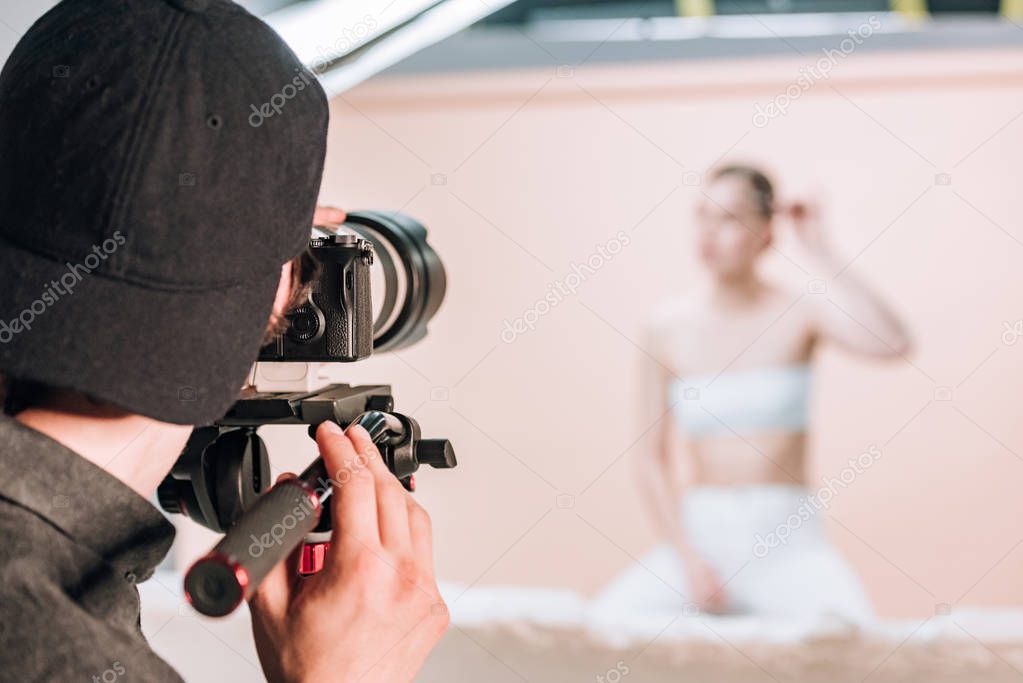 Rear view of videographer with camera working with woman in photo studio