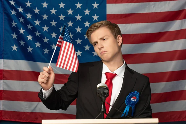 Displeased man on tribune and holding american flag — Stock Photo