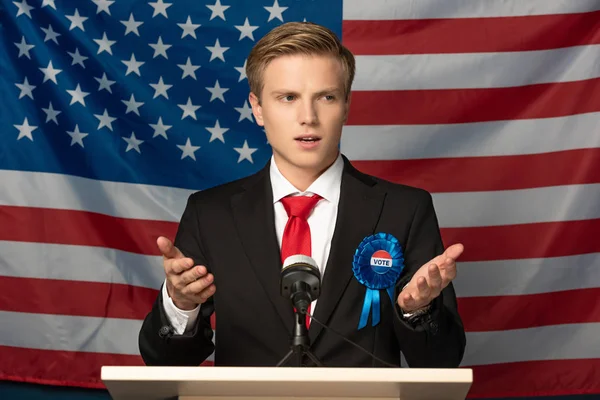 Emotionaler Mann auf der Tribüne während einer Rede vor dem Hintergrund der amerikanischen Flagge — Stockfoto