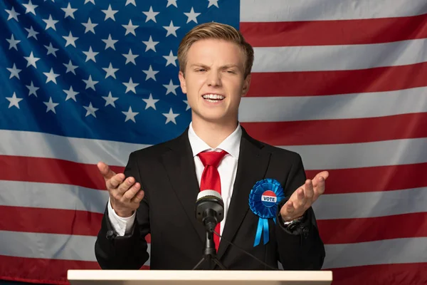 Hombre emocional en tribuna durante discurso sobre fondo de bandera americana — Stock Photo