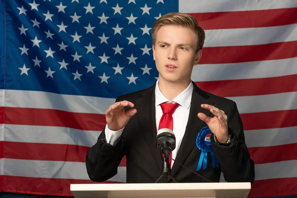 Emotionaler Mann auf der Tribüne während einer Rede vor dem Hintergrund der amerikanischen Flagge — Stockfoto