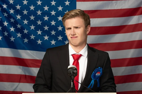 Verwirrter Mann auf Tribüne vor Hintergrund amerikanischer Flagge — Stockfoto
