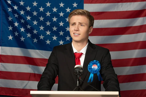 Selbstbewusster emotionaler Mann auf der Tribüne vor amerikanischem Flaggenhintergrund — Stockfoto