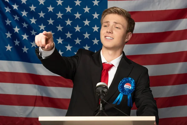 Confident man pointing with finger on tribune on american flag background — Stock Photo