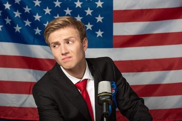 Verwirrter Mann auf Tribüne vor Hintergrund amerikanischer Flagge — Stockfoto