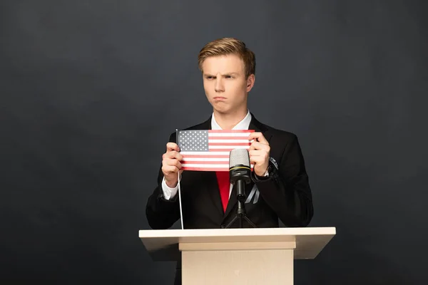 Розгніваний емоційний чоловік на трибуні з американським прапором на чорному тлі — стокове фото