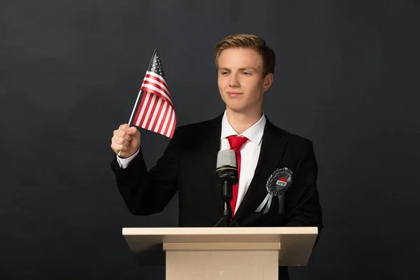 Uomo emotivo sorridente su tribuna con bandiera americana su sfondo nero — Foto stock