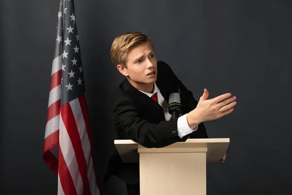 Emotionaler Mann gestikuliert auf Tribüne mit amerikanischer Flagge auf schwarzem Hintergrund — Stockfoto