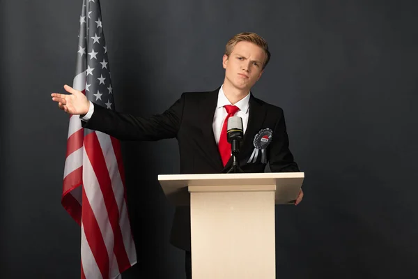 Displeased emotional man on tribune with american flag on black background — Stock Photo