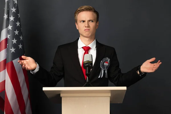 Dissatisfied emotional man on tribune with american flag on black background — Stock Photo