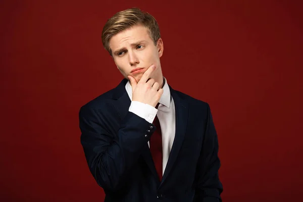 Thoughtful man in suit on red background — Stock Photo