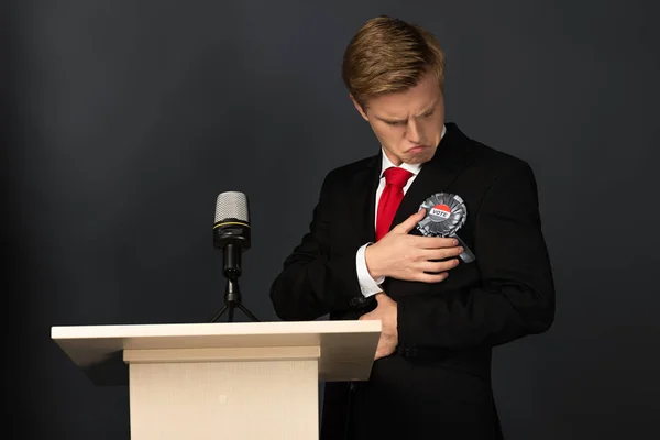 Emotionaler Mann blickt auf Abzeichen auf Tribüne auf schwarzem Hintergrund — Stockfoto