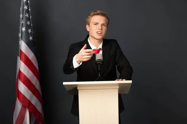 Эмоциональный человек выступает на трибуне с американским флагом на черном фоне — стоковое фото