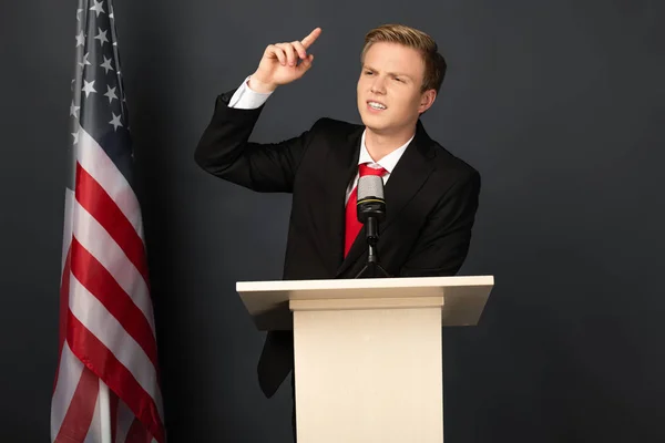 Uomo emotivo parlando su tribuna con bandiera americana su sfondo nero — Foto stock