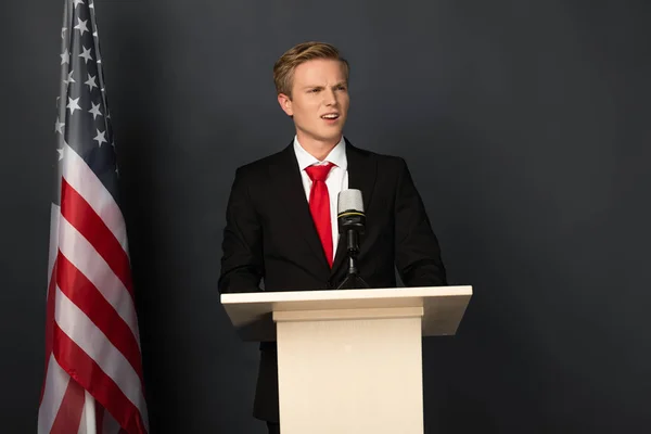 Hombre emocional hablando en tribuna con bandera americana sobre fondo negro - foto de stock
