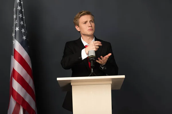 Emotionaler Mann spricht auf Tribüne mit amerikanischer Flagge auf schwarzem Hintergrund — Stockfoto