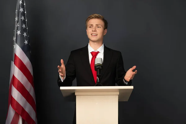 Uomo emotivo parlando su tribuna con bandiera americana su sfondo nero — Foto stock