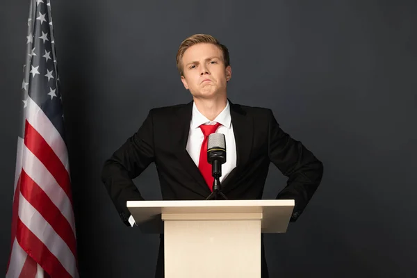 Confiante homem emocional na tribuna com bandeira americana em fundo preto — Fotografia de Stock