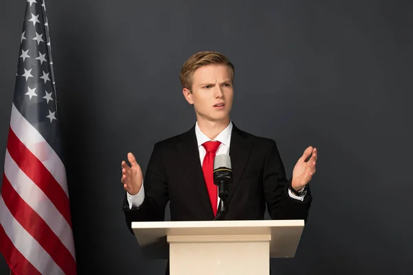 Emotionaler Mann gestikuliert auf Tribüne mit amerikanischer Flagge auf schwarzem Hintergrund — Stockfoto