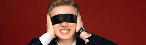 Man with blindfold on eyes covering ears with hands on red background — Stock Photo