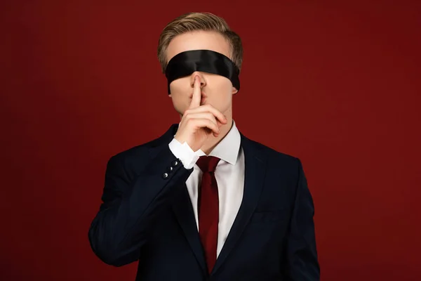 Homme avec les yeux bandés montrant un geste shh sur fond rouge — Photo de stock