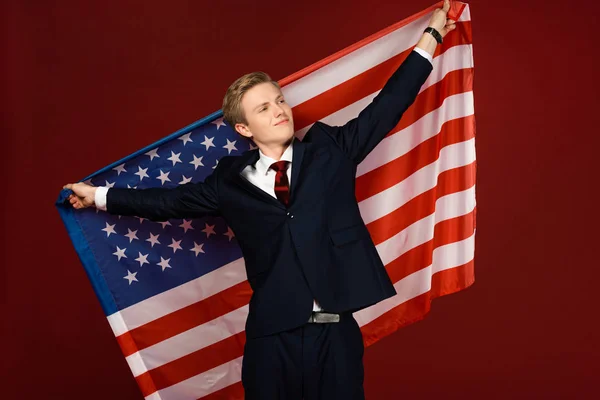 Sorrindo homem segurando bandeira americana no fundo vermelho — Fotografia de Stock