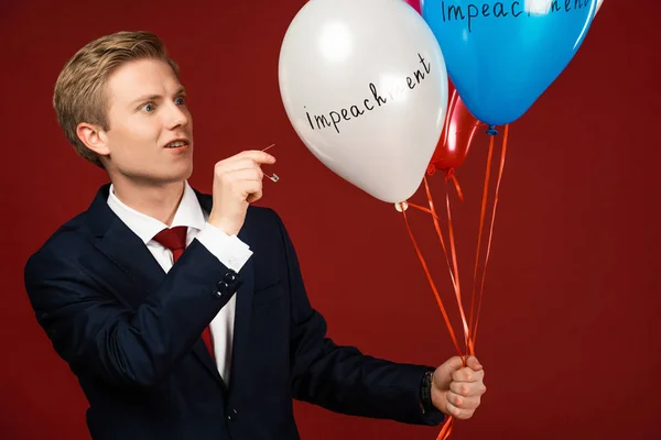 Hombre emocional estallando globos con letras de juicio político sobre fondo rojo - foto de stock