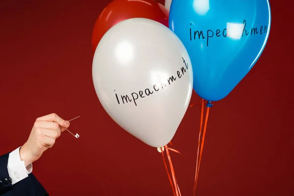 Vista cortada do homem estourando balões com letras de impeachment no fundo vermelho — Fotografia de Stock
