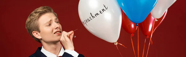 Emotionaler Mann platzt Luftballons mit Amtsenthebungsschrift auf rotem Hintergrund — Stockfoto