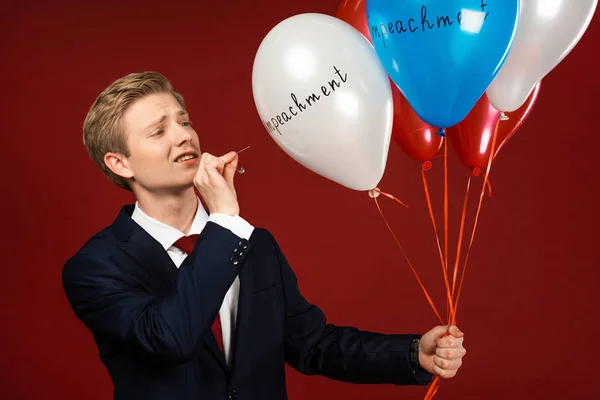 Hombre emocional estallando globos con letras de juicio político sobre fondo rojo - foto de stock