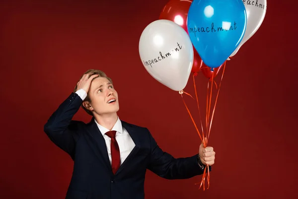 Worried man holding balloons with impeachment lettering on red background — Stock Photo