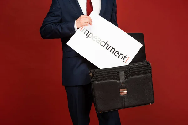 Vista recortada del hombre tomando tarjeta blanca con letras de juicio político de la caja de cuero sobre fondo rojo — Stock Photo