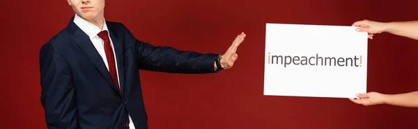 Vista recortada del hombre que no muestra ningún gesto a la tarjeta blanca con letras de juicio político sobre fondo rojo - foto de stock