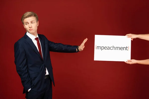 Homem emocional mostrando nenhum gesto para cartão branco com letras de impeachment no fundo vermelho — Fotografia de Stock