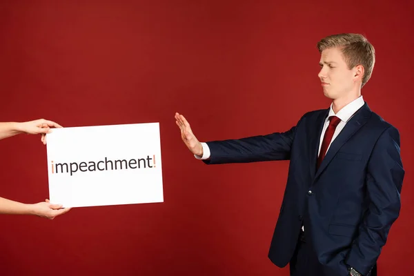 Homem emocional mostrando nenhum gesto para cartão branco com letras de impeachment no fundo vermelho — Fotografia de Stock