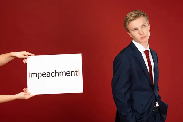 Skeptical man near white card with impeachment lettering on red background — Stock Photo