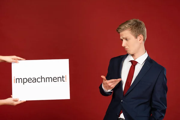 Homem cético olhando para o cartão branco com letras de impeachment no fundo vermelho — Fotografia de Stock